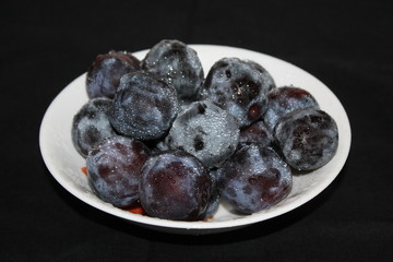 ripe plum with blue splashes on the plate isolated on black background