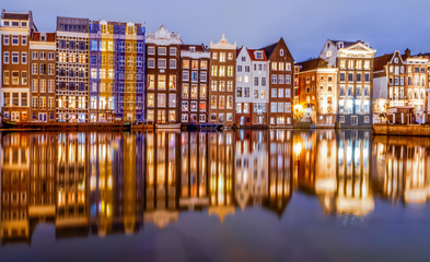 Fototapeta na wymiar Scenic night view of traditional colourful old houses and boats with reflection on canal Damrak in the old city of Amsterdam, Netherlands.