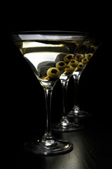 Three Martini drinks with olives on stick isolated on black table