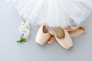 Ballet pointe shoes and white tutu skirt on gray background with blooming cherry flowers. Concept of dance, spring, ballet school, ballerinas clothes, stuff and things. Top view, flat lay.
