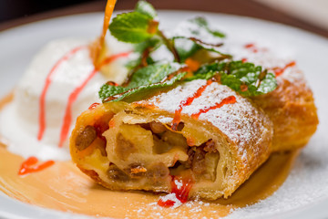 piece of strudel with apples on a white plate with powdered sugar and mint