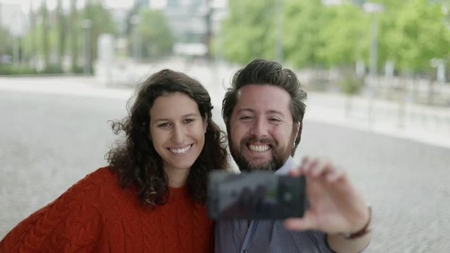 Happy couple taking selfie outdoor. Smiling bearded man and young woman standing together on street and taking pictures via smartphone. Technology concept