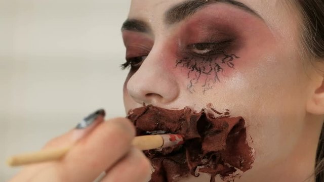 Halloween make-up. An image of a scary lady with a bloody mouth. The makeup artist's hand brushes the model's lips with a brush.
