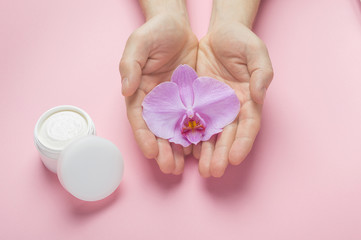 Obraz na płótnie Canvas Muscular man hands with natural manicure nails holding orchid flower. Man hands and body skin cosmetic care. White plastic jar with body cream. Mockup for natural herbal man cosmetics.