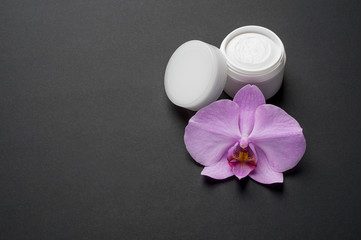 Fototapeta na wymiar Mockup cosmetic cream with herbal flowers for face, skin and body care hygiene moisture lotion wellness therapy mask in plastic jar on black background with orchid flower and copy space.