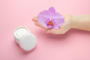 Fototapeta na wymiar Mockup for body skin care natural cosmetics. Woman hold orchid flower in hand on a pink background. Natural organic cosmetics with flowers extract. Beauty, fashion, cosmetology and spa concept.