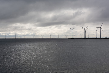 wind turbines standing tall and proud across the horizon. Grey overcast weather that makes a dramatic grey scale picture of green energy