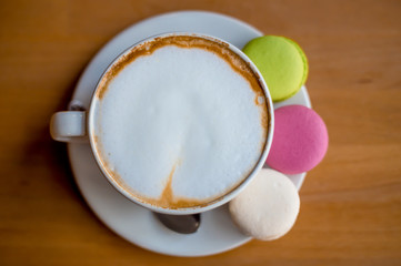 Tasty sweet colorful macarons and capuccino coffee white cup. Macaroons on wooden background. Top view. Space for text