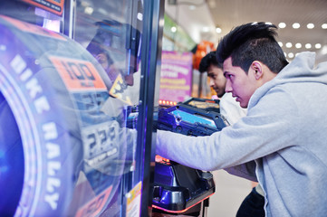 Two asian guys compete on shooter simulator game arcade machine.