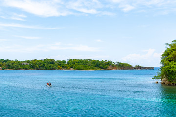 Tour boat with people sailing the beautiful turquoise ocean waters by Monkey Island (aka Pellew/Pelew/Pelu/ Princess Island) in San San, Port Antonio, off the coast of Portland Parish in Jamaica.