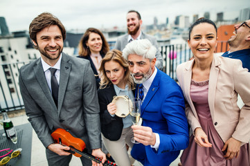 A group of joyful businesspeople having a party outdoors on roof terrace in city.