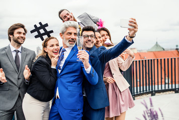 A group of joyful businesspeople outdoors on roof terrace in city, taking selfie on party.