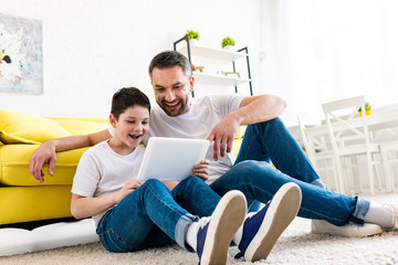 father and son sitting on carpet and using Digital Tablet in Living Room
