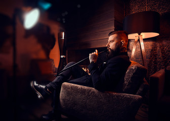 Fototapeta na wymiar Handsome bearded man is relaxing on lounge while smoking hookah. He has tattoo on his hand.