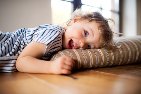 A toddler girl lying on the floor indoors at home, playing.