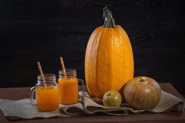 Fresh pumpkin juice and pumpkin on a burlap on a wooden table.