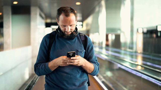 Man, tourist texting on smartphone riding escalator stairs at airport