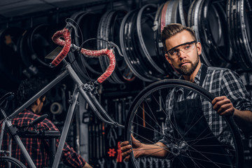 Fototapeta na wymiar Focused attractive man in glasses is chainging wheel for bicycle at busy workshop.