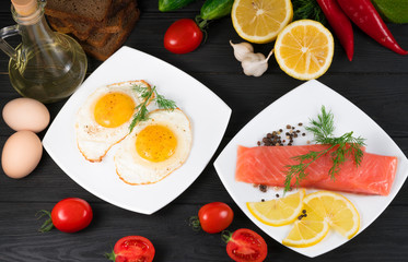 red fish, fried eggs with vegetables on a black wooden background