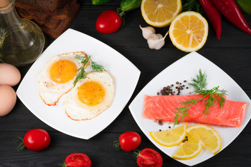 red fish, fried eggs with vegetables on a black wooden background