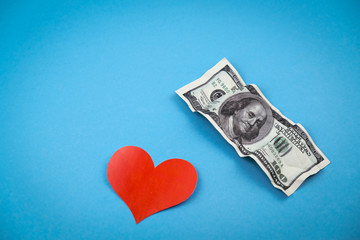 Red heart shape and 100 dollar bills on blue background.