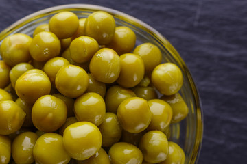 canned green peas in a glass bowl on a dark stone background