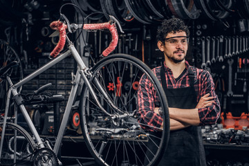 Smiling happy man in glasses is standing near fixed bicycle at his own workshop.