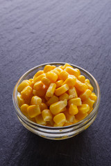 canned corn in a glass bowl on a dark stone background
