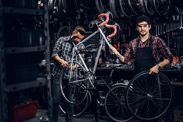 Good teamwork of two nice mans at busy bicycle workshop. Mans are wearing checkered shirts.