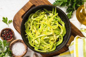 Zucchini noodles in frying pan on white.