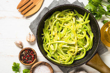 Zucchini noodles in frying pan on white.