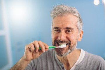 happy middle aged gray haired bearded man brushing his teeth