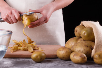 A young woman in an apron peeling potatoes