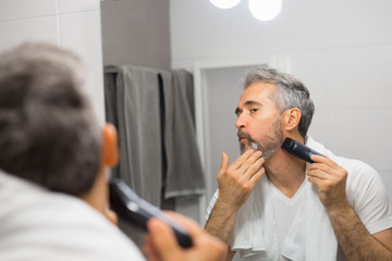 middle aged man trimming his beard in bathroom