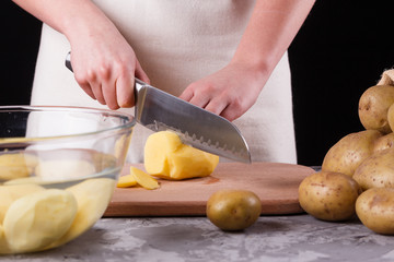 young woman in an apron cuts potatoes