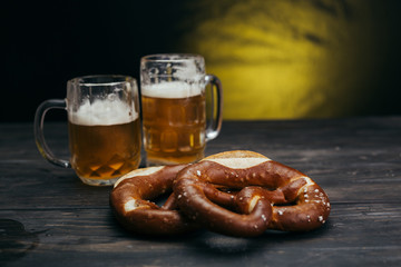 draft beer in the mugs and pretzels on dark wooden background