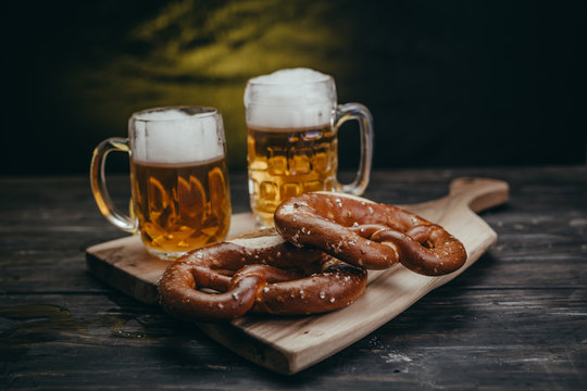 pretzels and draft beer on rustic cutting board against dark background