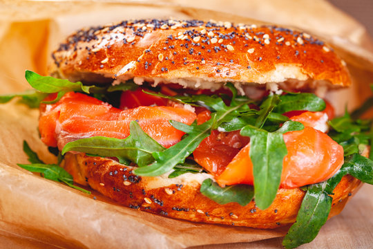 Bagel with cream cheese, smoked salmon and arugula salad in brown paper bag. Close up