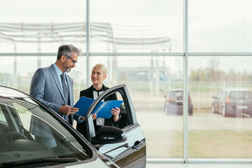 Naklejka na ściany i meble saleswoman showing car brochure ta a customer in car dealers showroom