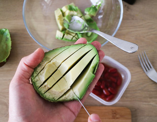Holding an avocado half in the hand, slicing avocado for a dip