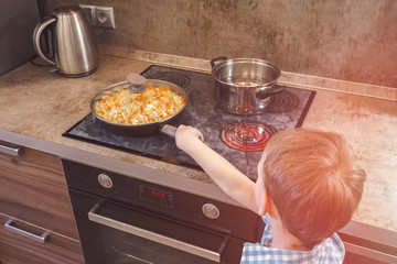 Little boy touches hot pan on the stove. Dangerous situation at home. Child on the kitchen