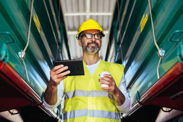worker in yellow protective wear using tablet and drinking coffee