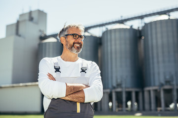middle aged agricultural worker standing crossed arms in front of grain silo © cherryandbees