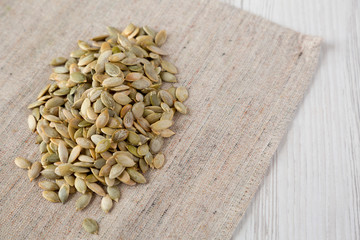Roasted pumpkin seeds on cloth over white wooden background, low angle view. Copy space.