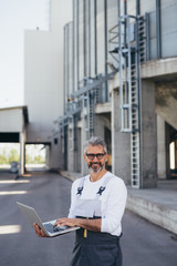 middle aged worker using laptop in front of grain silos