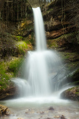 Close-up of sunlit, colorful forest waterfall at spring, flooding with water and sunlit, moss covered rocks 