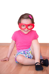 Little girl with toy eyeglasses and dance shoes sitting, isolated 