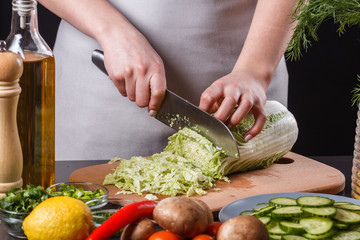 A young woman in a gray apron cuts chinese cabbage