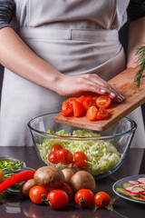 young woman in a gray apron adds cherry tomatoes to a salad