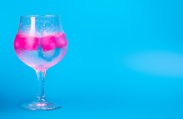 A cold drink with colorful pink and blue ice in a wine glass on a blue background. Summer concept image with copy space for text